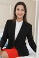 A woman in a black blazer and red skirt sitting on a bed.