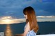 A woman with long red hair standing on a balcony overlooking the ocean.