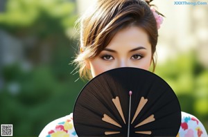 A woman holding a black fan in front of her face.