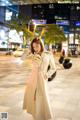 A woman in a white trench coat standing on a city street.